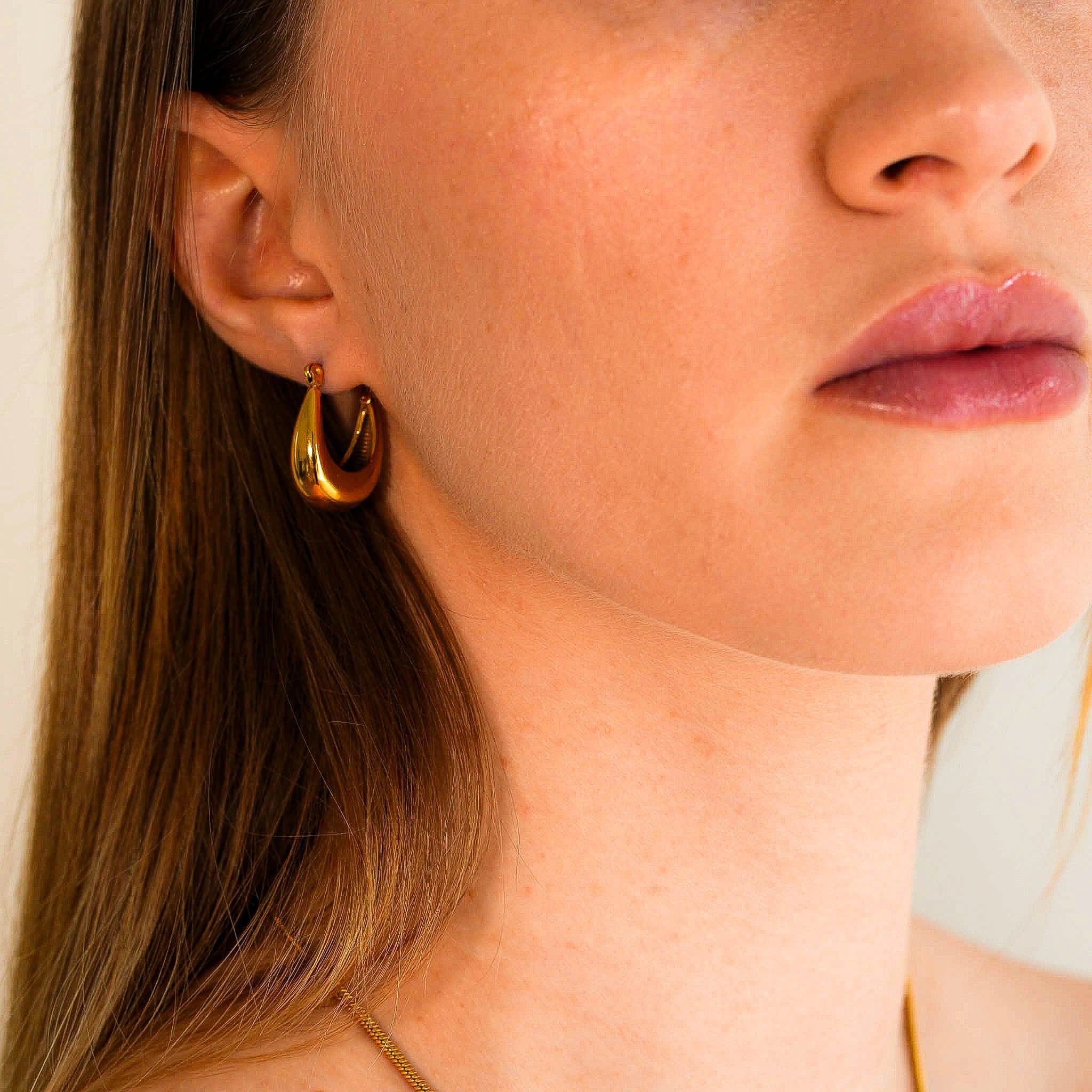 A woman wearing the Leona 18k gold plated earrings looking right